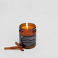 Transcend Cosmetics Cinnamon Cabin Organic Beeswax Candle in an amber glass jar with a wooden wick, burning with a warm flame, surrounded by Cinnamon sticks, highlighting its natural and soothing ingredients.